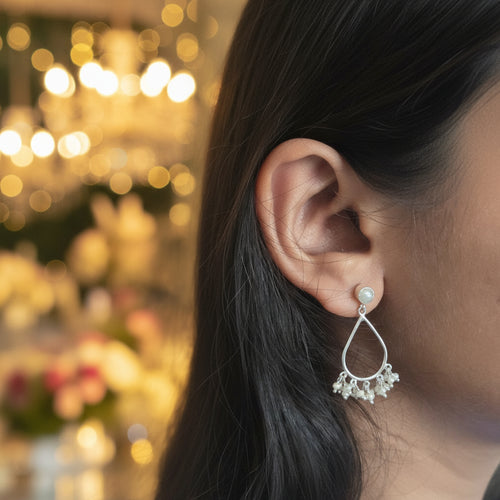 Silver earring with dangling beads worn by a person with dark hair.