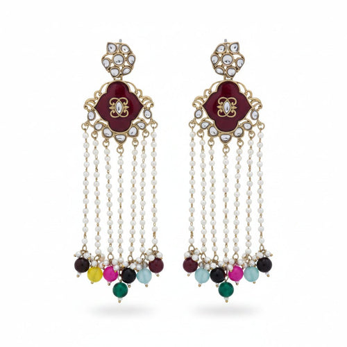 A pair of silver-toned Indian chandelier earrings with deep red floral enamel, clear stone accents, and dangling pearl-like chains ending in multicolored beads, displayed on a textured off-white fabric background.