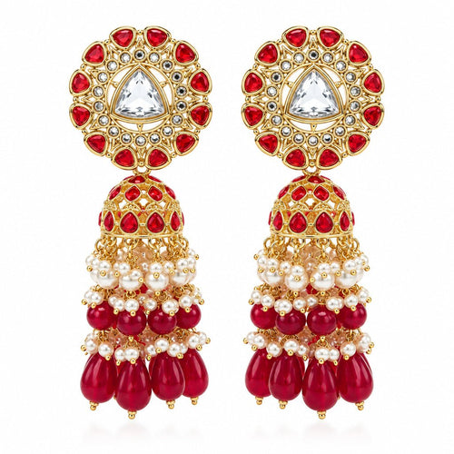 A pair of gold-plated Indian jhumka earrings decorated with red stones, white faux pearls, and a central clear stone, displayed on clear acrylic stands against a neutral gray background.