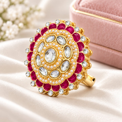 A gold-plated mandarin-style ring featuring a central clear oval stone surrounded by milky white pearls, clear round stones, and deep pinkish-red oval stones, all set in a polished gold-tone band on a white background.