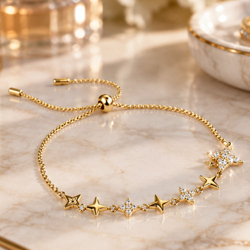 A delicate gold chain bracelet with a sliding adjustment clasp and a row of star-shaped charms, some embellished with clear rhinestones, displayed on a white surface with a dark red fabric accent.