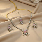 A silver-toned jewelry set featuring a necklace, matching earrings, and a dangling maang tikka, all adorned with pink stones and small clear stones, displayed on a white background with loose matching stone embellishments arranged around them.