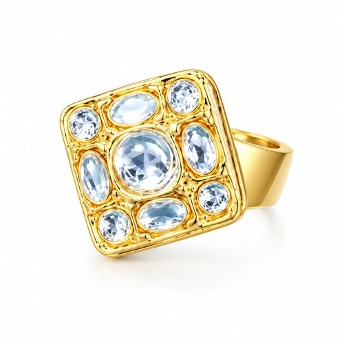 A square gold ring with clear gemstones, photographed on a dark teal textured surface.