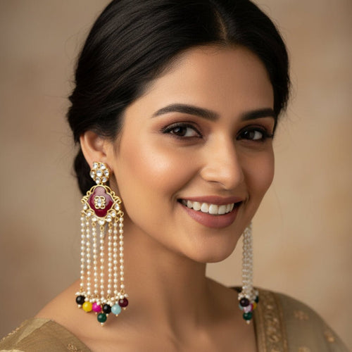 A pair of silver-toned Indian chandelier earrings with deep red floral enamel, clear stone accents, and dangling pearl-like chains ending in multicolored beads, displayed on a textured off-white fabric background.