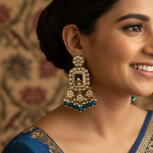 A close-up of a person wearing a large gold-toned traditional Indian dangle earring with white stones and blue bead accents.