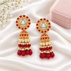 A pair of gold-plated Indian jhumka earrings decorated with red stones, white faux pearls, and a central clear triangular crystal on a white background.